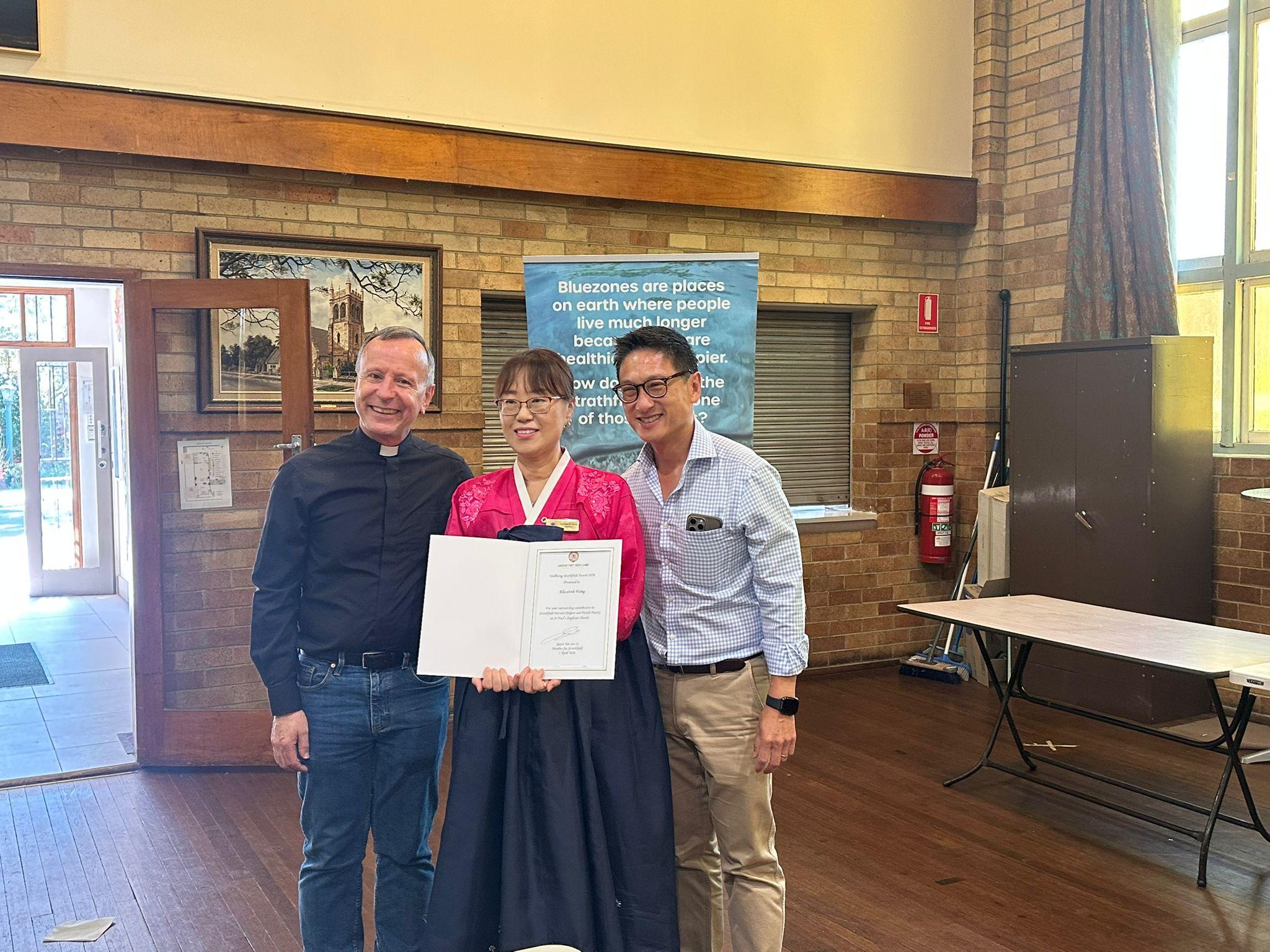 SMULC member in traditional dress receiving a Strathfield MP community service award certificate
