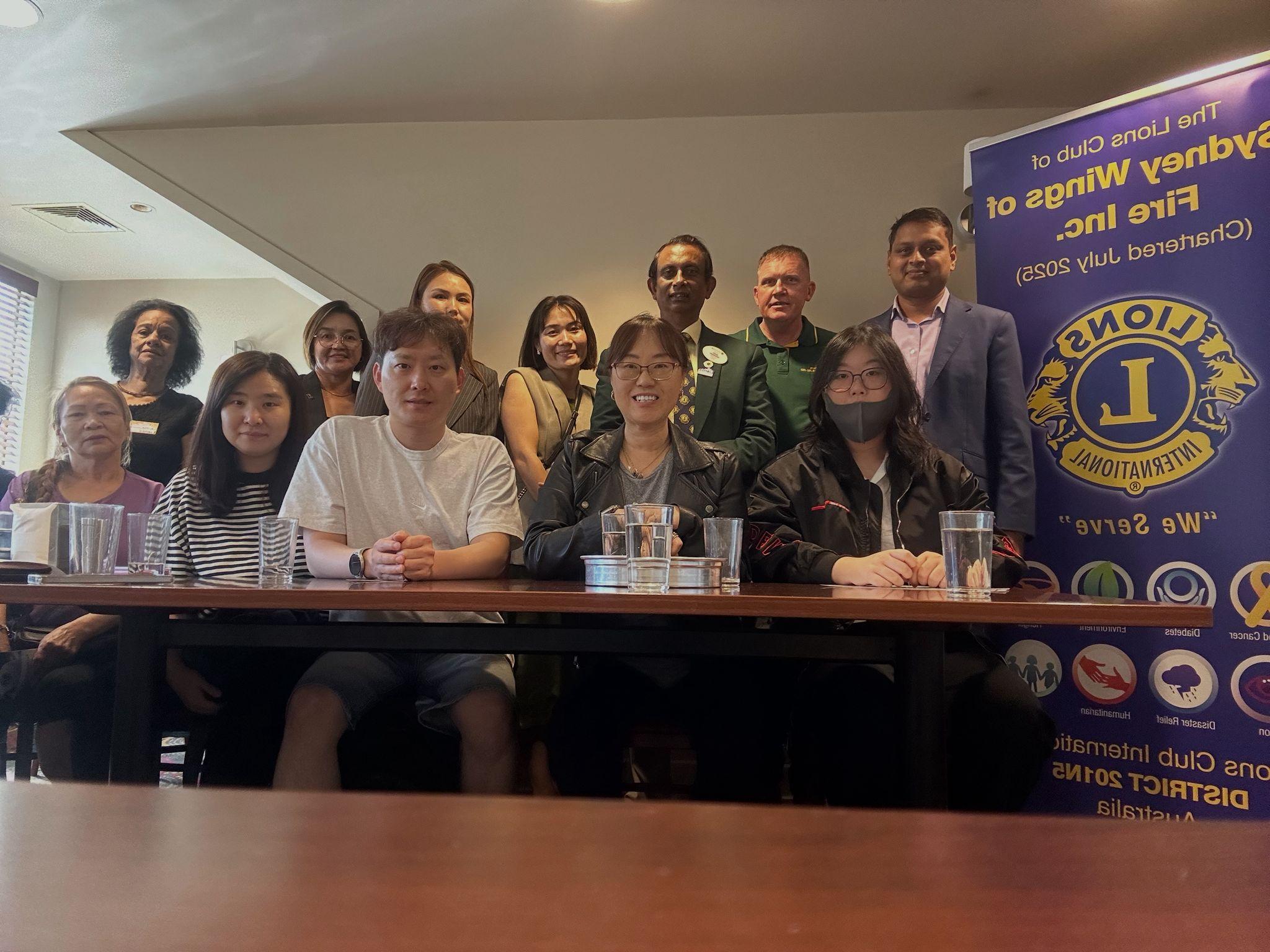SMULC charter members gathered around a meeting table with a Lions Club banner