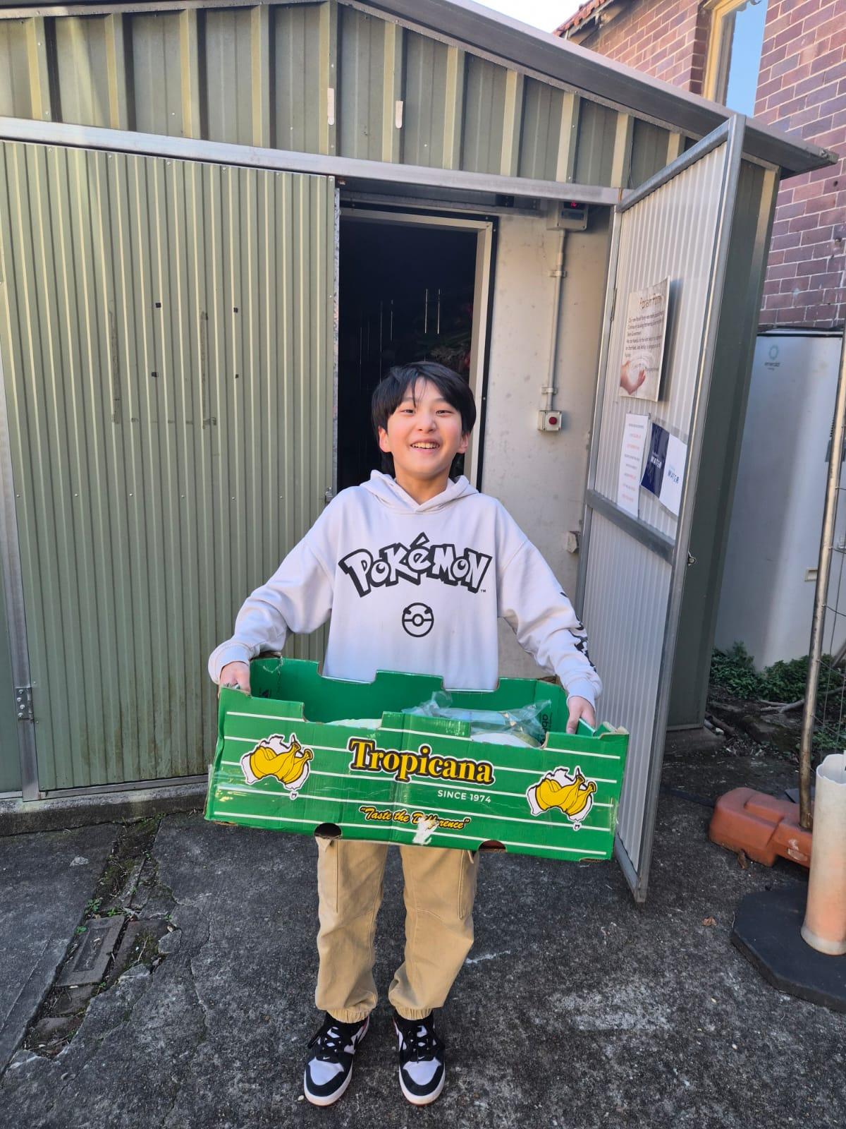 A young SMULC volunteer smiling while carrying a box of rescued produce at the community food pantry